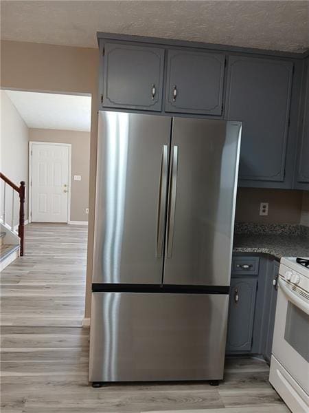 kitchen with freestanding refrigerator, white gas range, gray cabinets, light wood-type flooring, and dark countertops