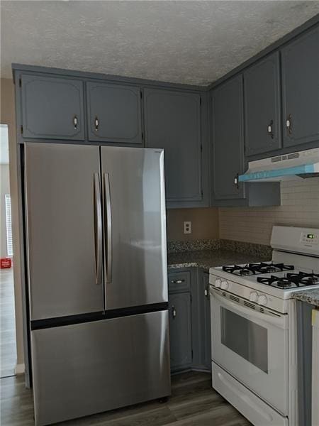 kitchen featuring freestanding refrigerator, white gas range oven, under cabinet range hood, dark wood finished floors, and gray cabinetry