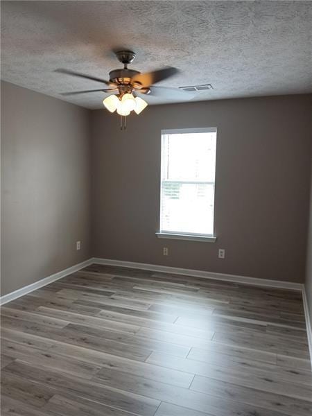 empty room with a ceiling fan, baseboards, wood finished floors, and a textured ceiling
