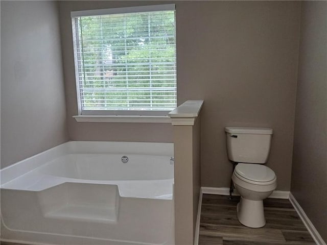 full bath featuring a garden tub, toilet, wood finished floors, and baseboards