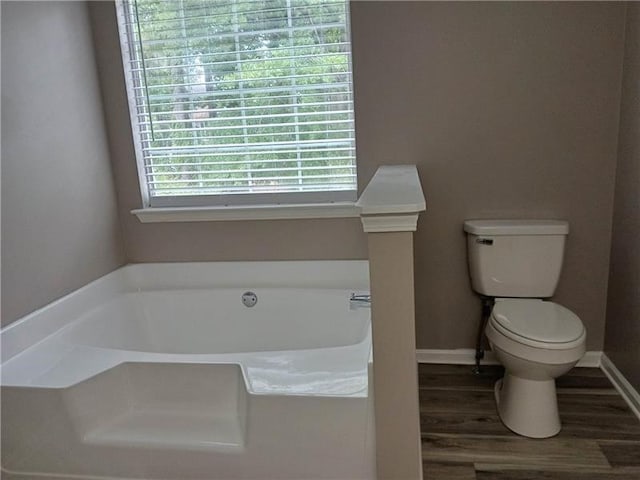 bathroom featuring toilet, a garden tub, wood finished floors, and baseboards