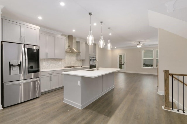 kitchen with pendant lighting, a center island with sink, wall chimney range hood, ceiling fan, and stainless steel appliances