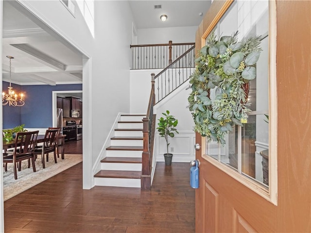 foyer entrance featuring coffered ceiling, dark wood-style floors, beamed ceiling, stairs, and a notable chandelier