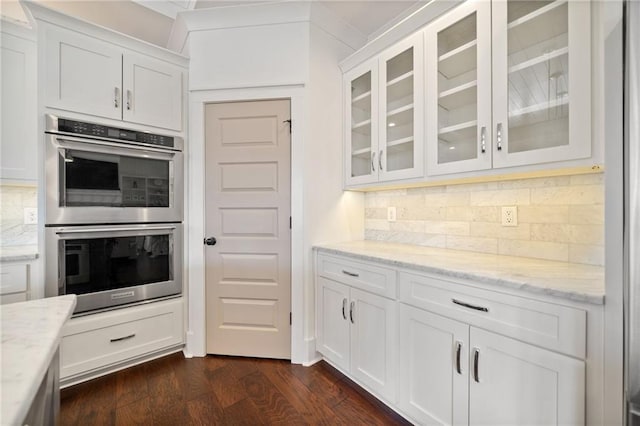 kitchen featuring white cabinetry, tasteful backsplash, light stone counters, dark hardwood / wood-style floors, and stainless steel double oven