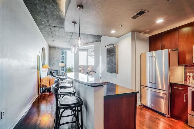 kitchen with appliances with stainless steel finishes, a kitchen island, decorative light fixtures, dark wood-type flooring, and a breakfast bar area