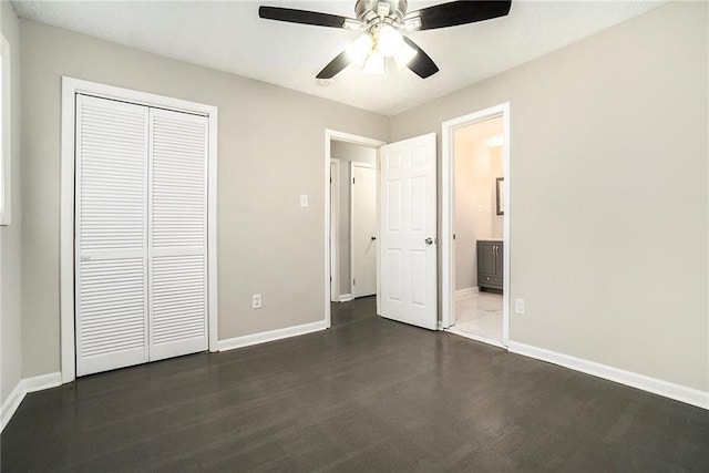 unfurnished bedroom with a closet, connected bathroom, dark wood finished floors, and baseboards