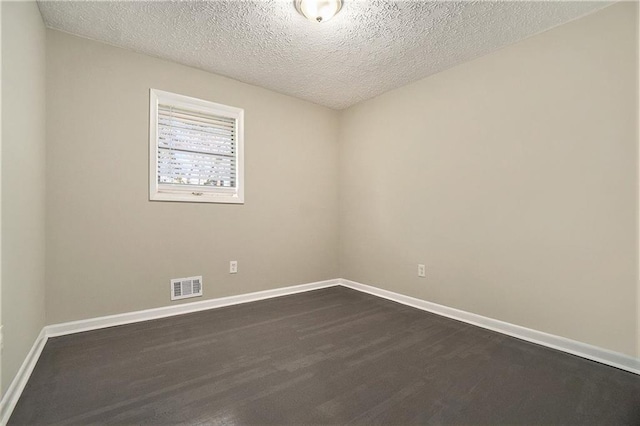 unfurnished room featuring dark wood-type flooring, visible vents, a textured ceiling, and baseboards