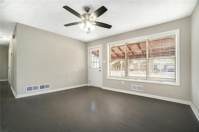 empty room with finished concrete floors, visible vents, a textured ceiling, and baseboards