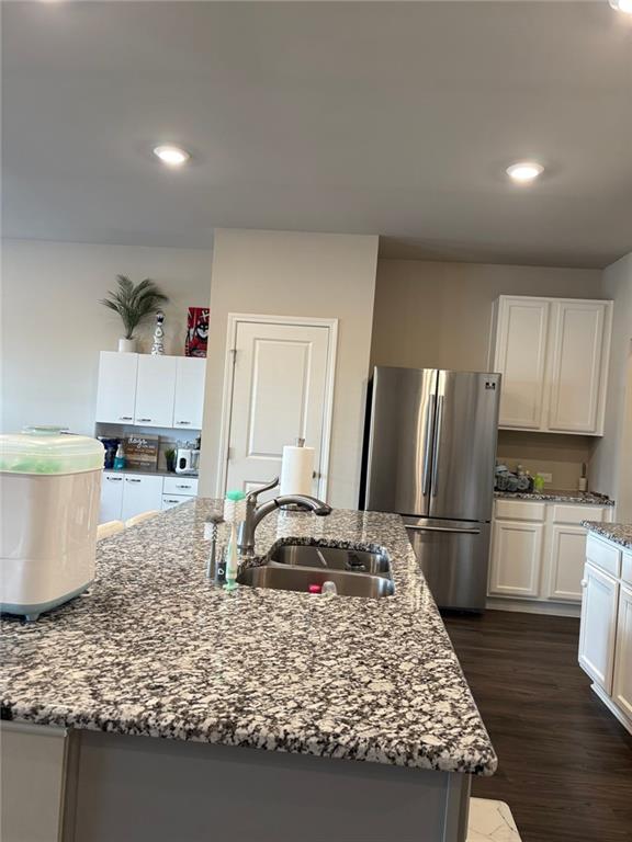 kitchen with light stone counters, a sink, white cabinets, freestanding refrigerator, and dark wood finished floors