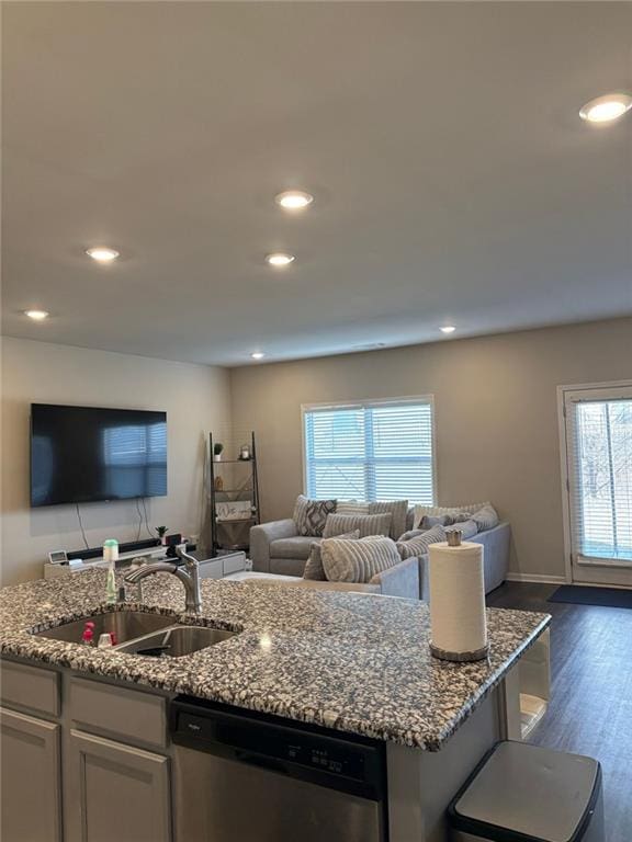 kitchen featuring an island with sink, light stone counters, open floor plan, stainless steel dishwasher, and a sink