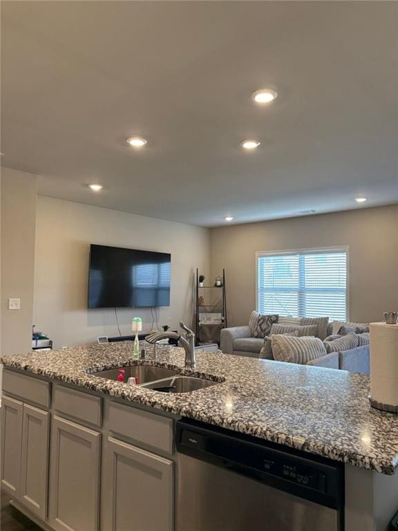 kitchen featuring open floor plan, stainless steel dishwasher, a sink, and light stone counters