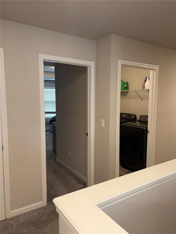 hall with baseboards, dark colored carpet, and washing machine and clothes dryer