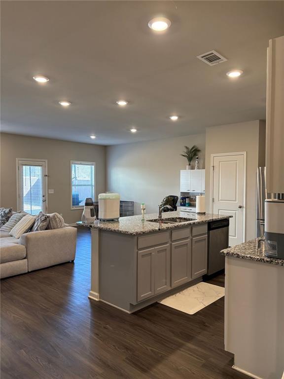 kitchen with a sink, visible vents, appliances with stainless steel finishes, light stone countertops, and a center island with sink