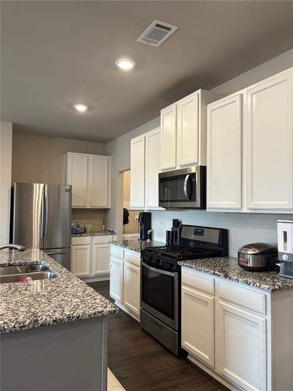 kitchen featuring stone counters, dark wood finished floors, visible vents, appliances with stainless steel finishes, and a sink