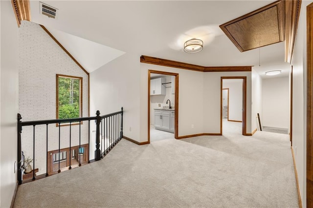 corridor with vaulted ceiling, brick wall, sink, crown molding, and light carpet