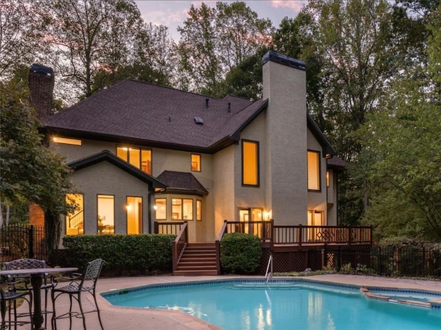 pool at dusk featuring an in ground hot tub, a deck, and a patio