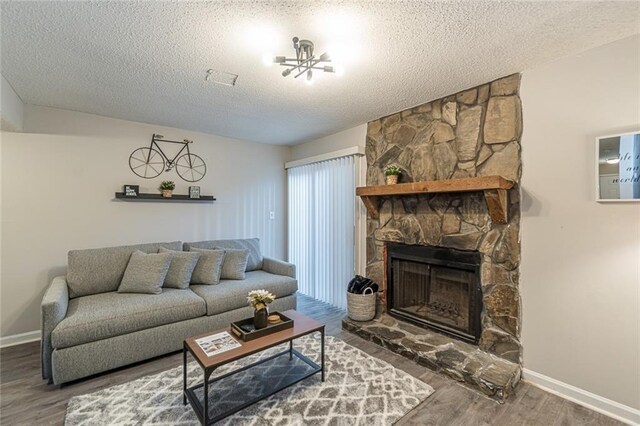 living room featuring hardwood / wood-style flooring, a textured ceiling, and a stone fireplace