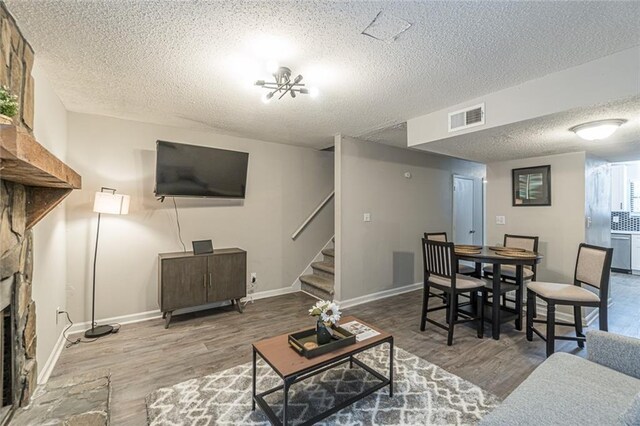 living room with a notable chandelier, a textured ceiling, wood-type flooring, and a fireplace