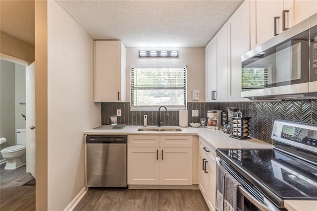 kitchen with appliances with stainless steel finishes, sink, hardwood / wood-style floors, white cabinetry, and decorative backsplash