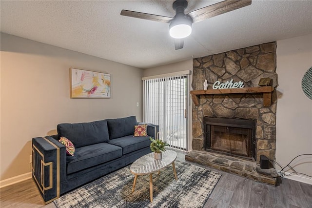 living room with ceiling fan, hardwood / wood-style flooring, a textured ceiling, and a stone fireplace