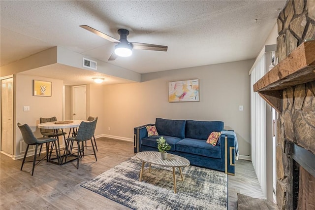 living room featuring a textured ceiling, a fireplace, light hardwood / wood-style floors, and ceiling fan