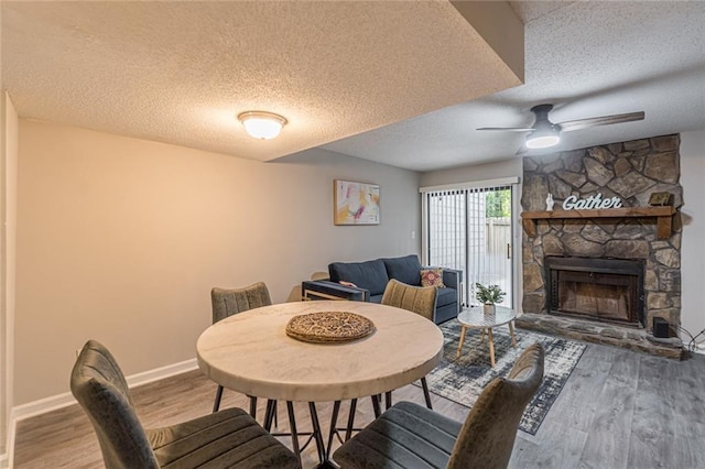 dining room featuring ceiling fan, hardwood / wood-style flooring, a textured ceiling, and a stone fireplace