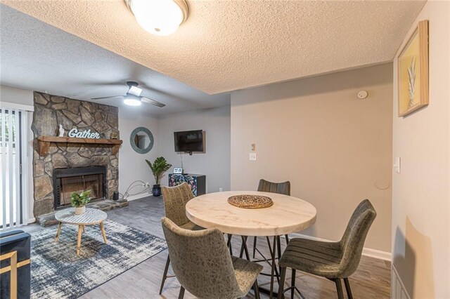 dining area featuring light hardwood / wood-style floors, a textured ceiling, a fireplace, and ceiling fan