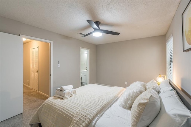 carpeted bedroom featuring a closet, a textured ceiling, ensuite bathroom, and ceiling fan