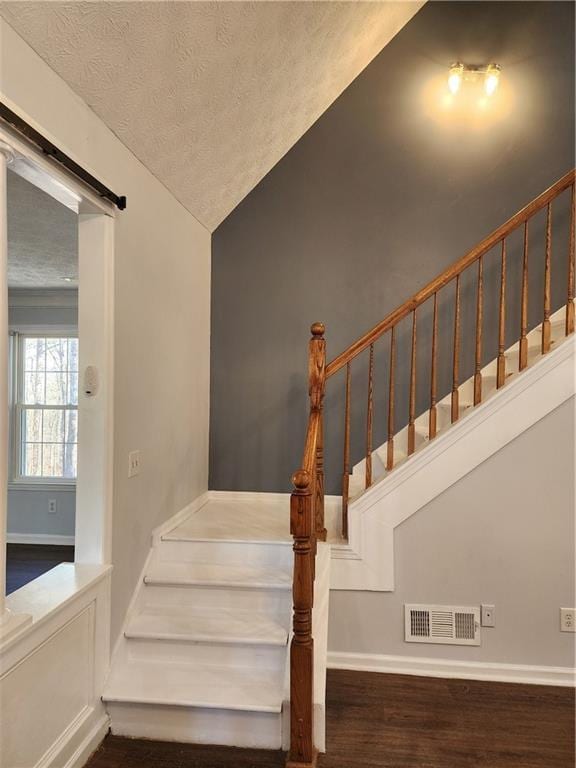 stairs featuring wood-type flooring, a barn door, lofted ceiling, and a textured ceiling