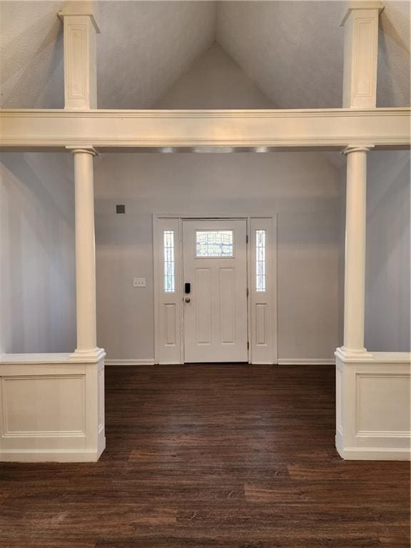 foyer entrance featuring dark hardwood / wood-style flooring, vaulted ceiling, and ornate columns