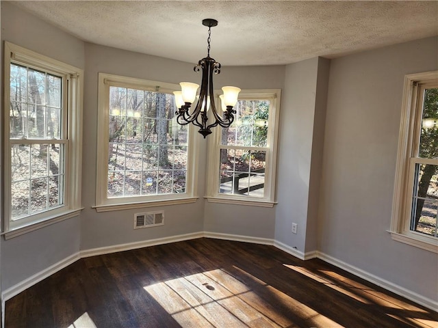 unfurnished dining area with dark wood-type flooring, an inviting chandelier, and a textured ceiling