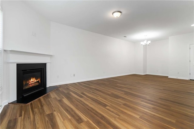 unfurnished living room featuring a chandelier, wood finished floors, a glass covered fireplace, and baseboards