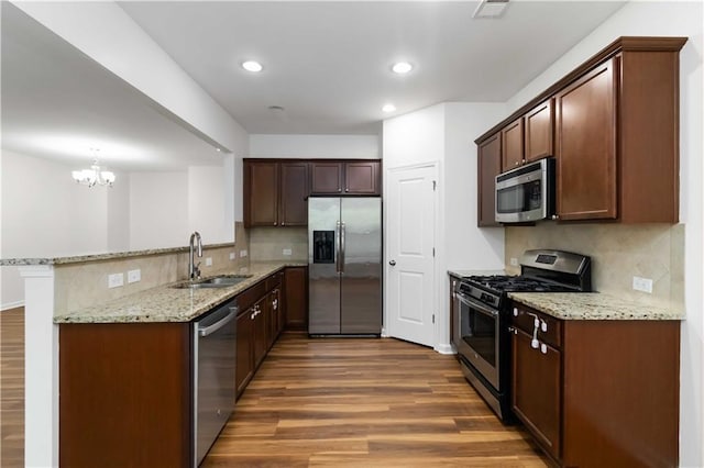 kitchen featuring stainless steel appliances, a sink, dark wood-type flooring, tasteful backsplash, and light stone countertops