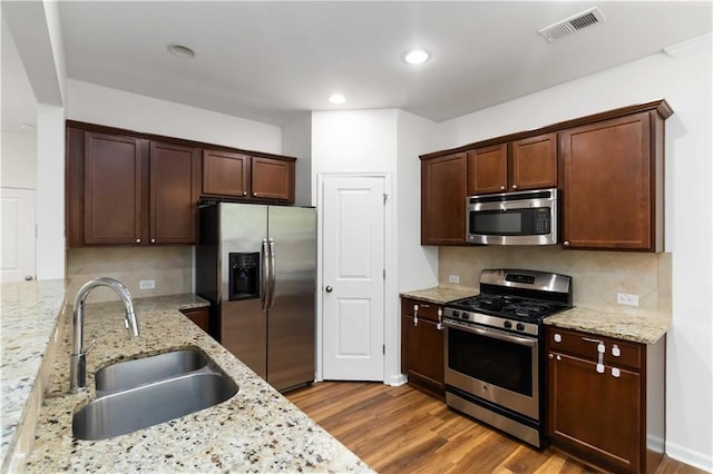 kitchen featuring appliances with stainless steel finishes, a sink, backsplash, light stone countertops, and recessed lighting