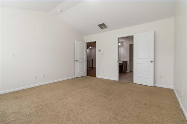 unfurnished bedroom featuring light carpet, baseboards, vaulted ceiling, and connected bathroom