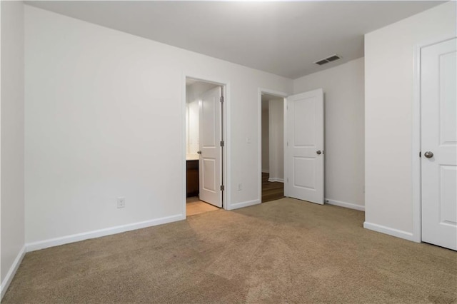 unfurnished bedroom with carpet flooring, baseboards, and ensuite bath