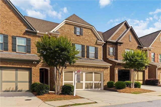 multi unit property featuring brick siding, a garage, driveway, and roof with shingles