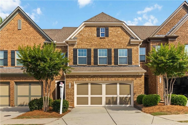 townhome / multi-family property with concrete driveway, brick siding, and roof with shingles