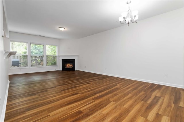 unfurnished living room featuring a chandelier, wood finished floors, baseboards, and a warm lit fireplace
