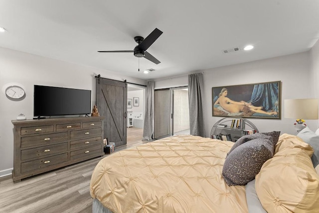 bedroom featuring a barn door, light wood-style flooring, ceiling fan, connected bathroom, and recessed lighting