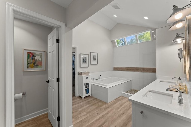 bathroom featuring wood finished floors, a bath, lofted ceiling, double vanity, and a spacious closet