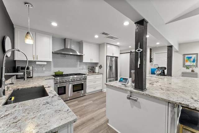 kitchen featuring wall chimney range hood, stainless steel appliances, a sink, backsplash, and white cabinetry