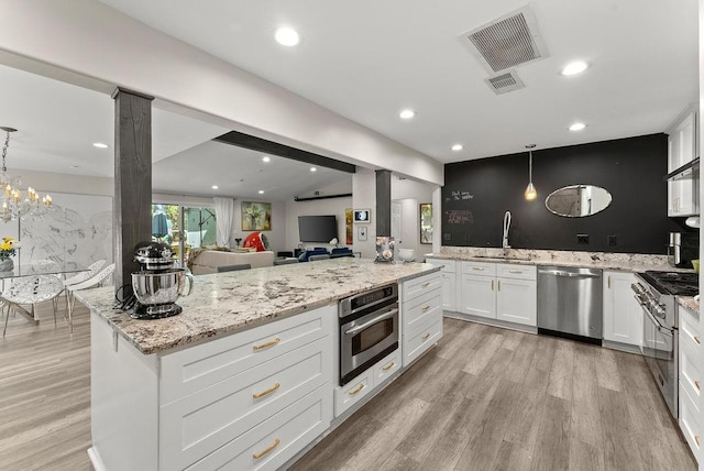 kitchen featuring stainless steel appliances, a sink, light stone counters, white cabinetry, and open floor plan