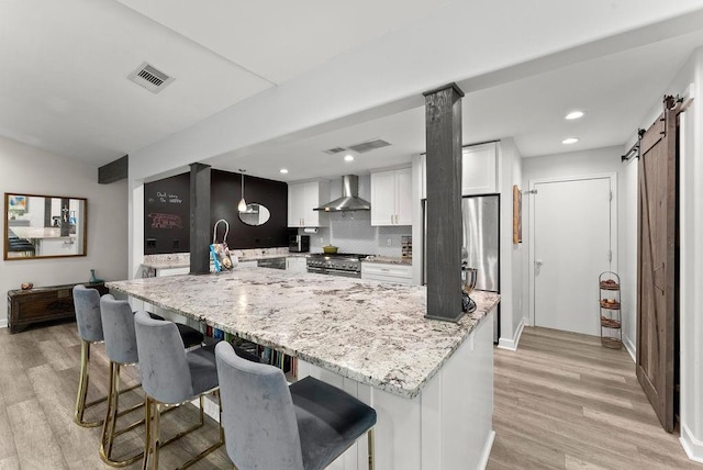 kitchen with wall chimney exhaust hood, stainless steel appliances, light wood finished floors, white cabinets, and backsplash