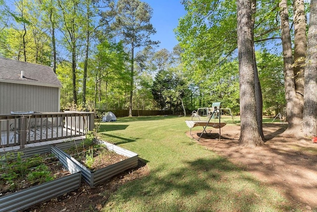 view of grassy yard featuring a vegetable garden, a deck, and view of scattered trees