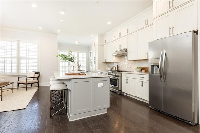 kitchen with backsplash, crown molding, under cabinet range hood, stainless steel appliances, and dark wood-style flooring