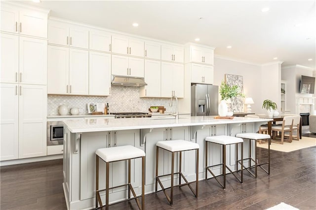 kitchen featuring under cabinet range hood, backsplash, dark wood finished floors, appliances with stainless steel finishes, and light countertops