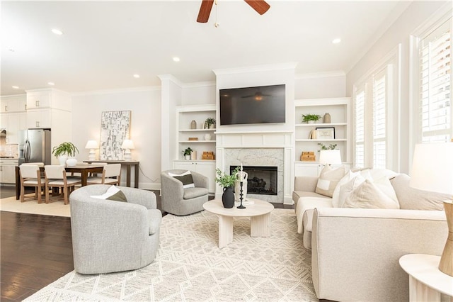 living area featuring ornamental molding, a ceiling fan, a high end fireplace, recessed lighting, and light wood finished floors