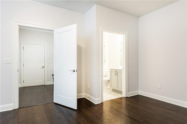 unfurnished bedroom featuring ensuite bath, baseboards, and wood finished floors