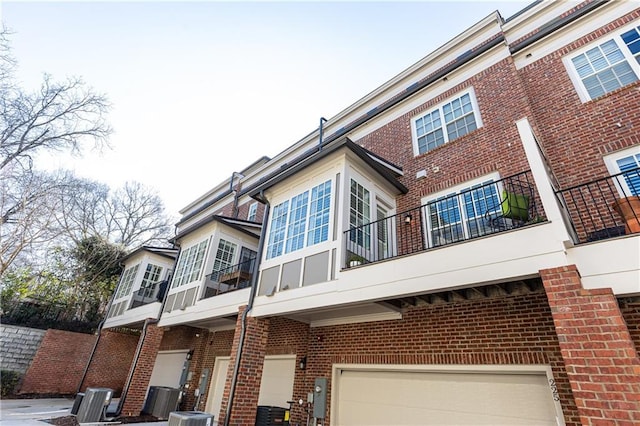 back of property with an attached garage, cooling unit, and brick siding